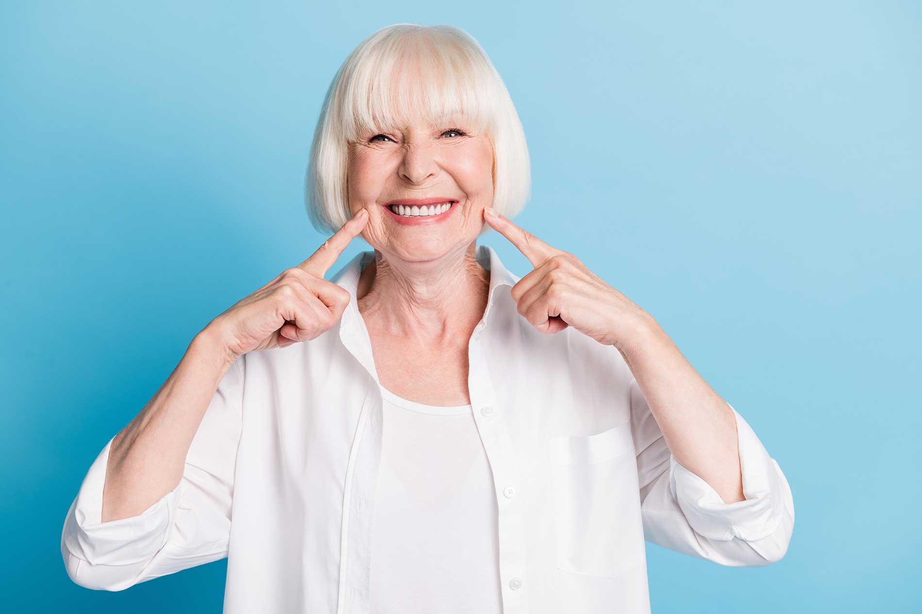 elderly woman smiling while pointing at her teeth